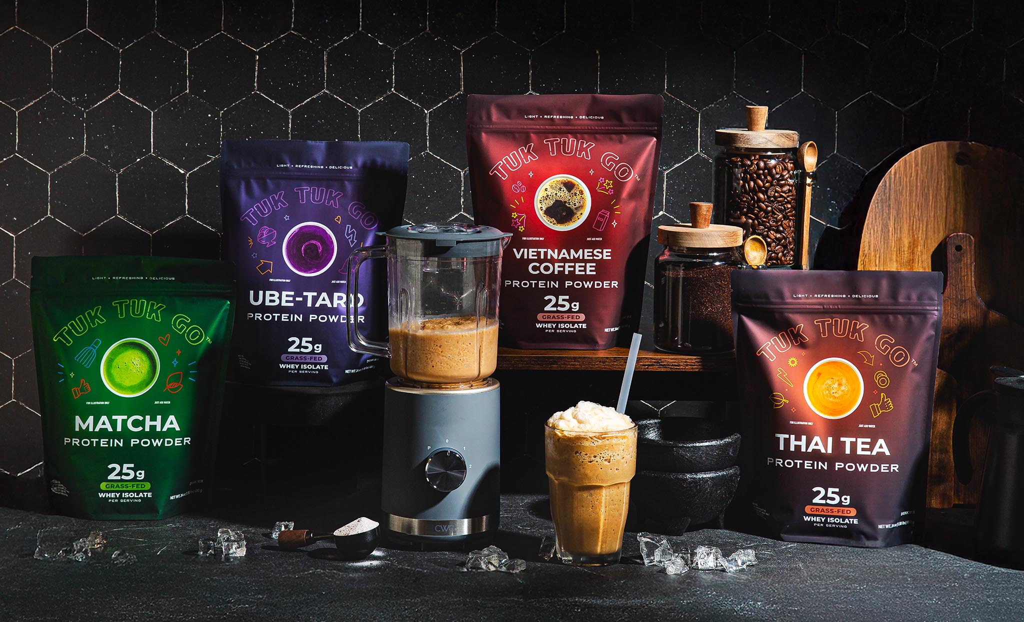 All four protein powder pouches on kitchen counter, with blender and glass of mixed protein drink.
