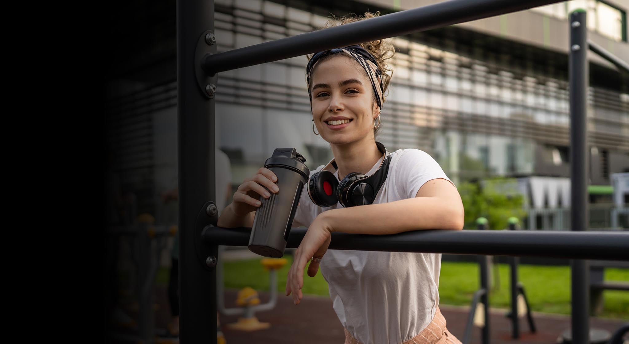 Header a woman in workout clothes with a shaker bottle at outdoor gym.