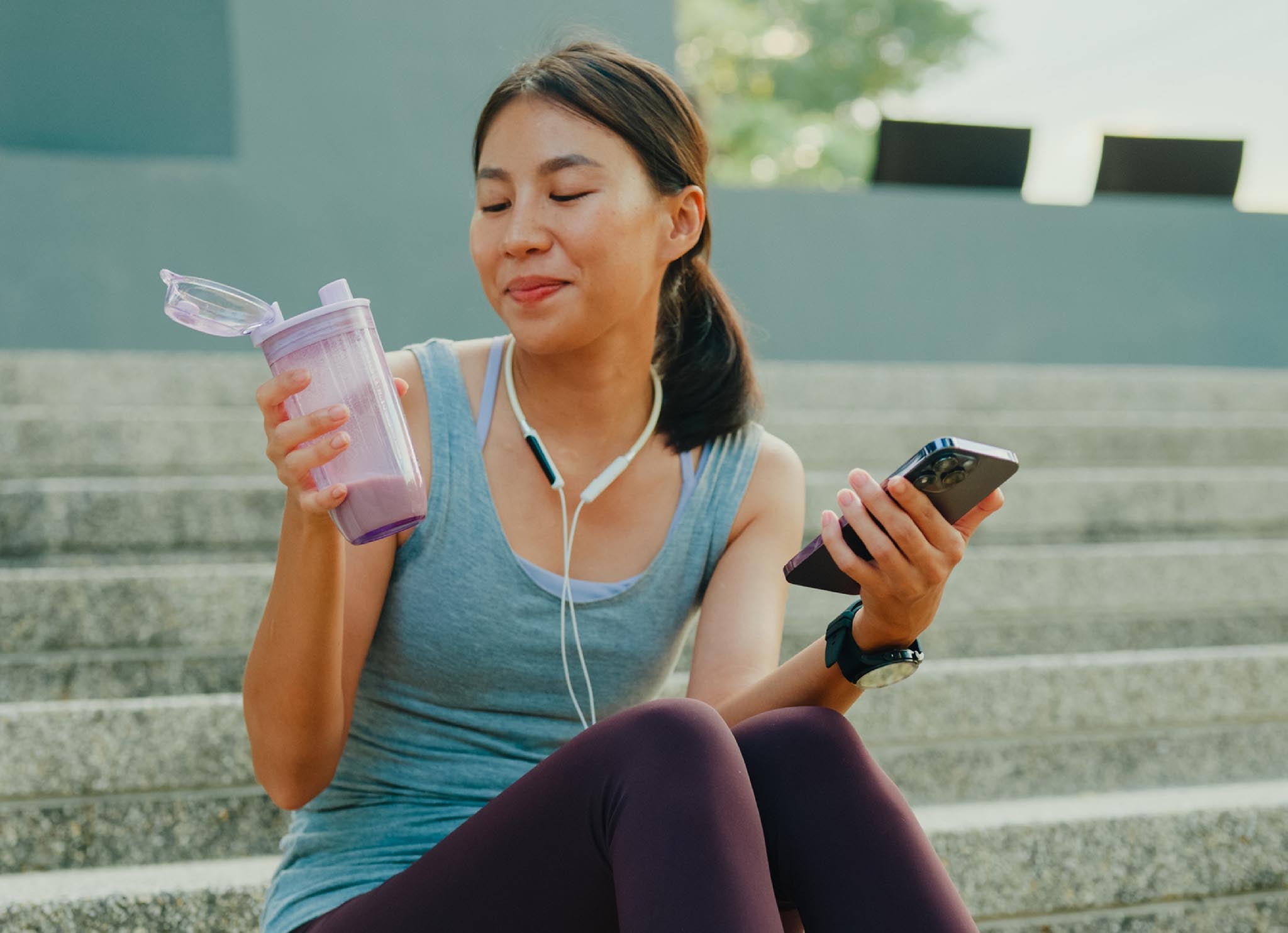 Young woman in workout gear with shaker bottle and headphones.